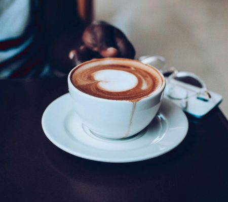 A delicious cappuccino with heart-shaped latte art served in a white cup on a saucer.
