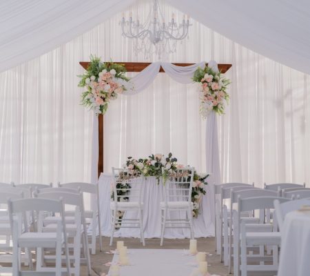 Beautiful wedding ceremony setup with white drapery, floral arrangements, and chandelier. Perfect for elegant nuptials.