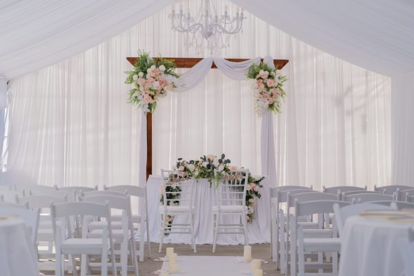 Beautiful wedding ceremony setup with white drapery, floral arrangements, and chandelier. Perfect for elegant nuptials.