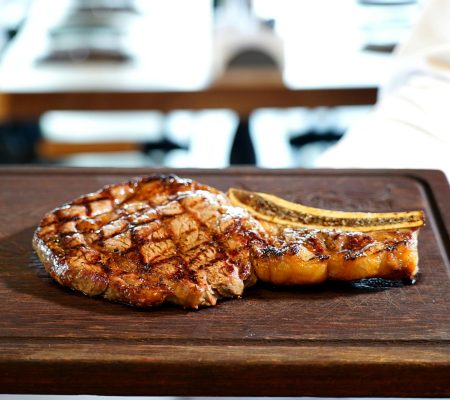 Close-up of a perfectly grilled steak and rib served on a wooden board indoors.